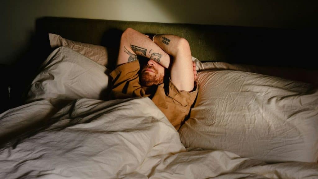A worried man lies in bed with his arm over his face, unable to sleep.