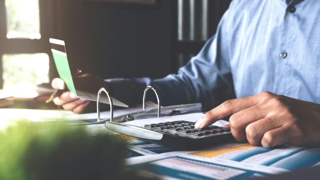 A person's hands press a calculator on a desk full of paperwork.