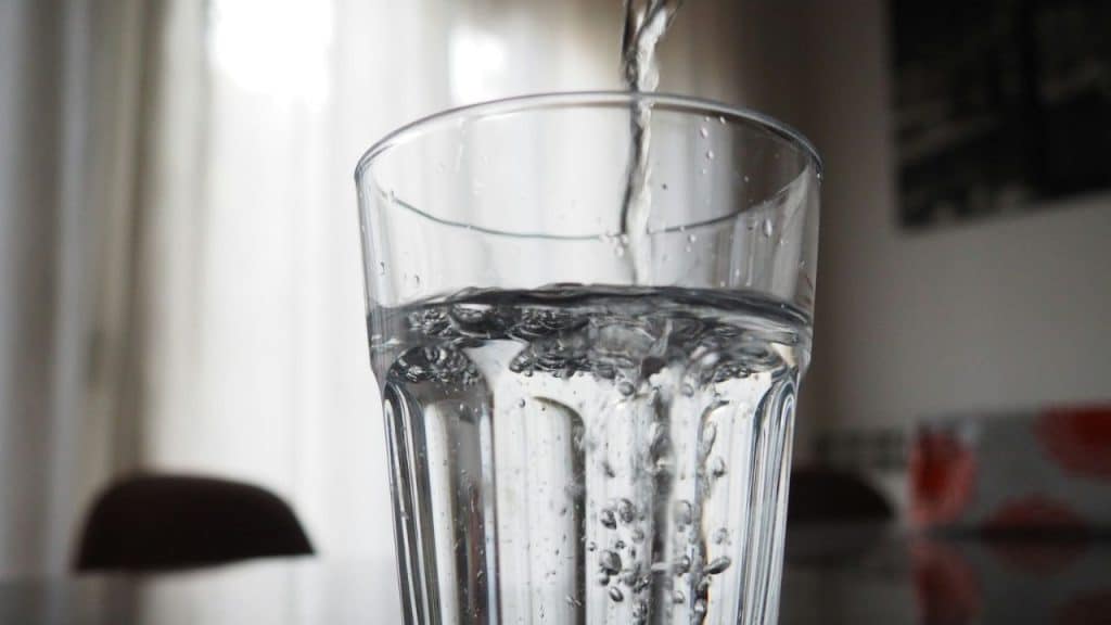 A stream of water is being poured into a clear drinking glass.