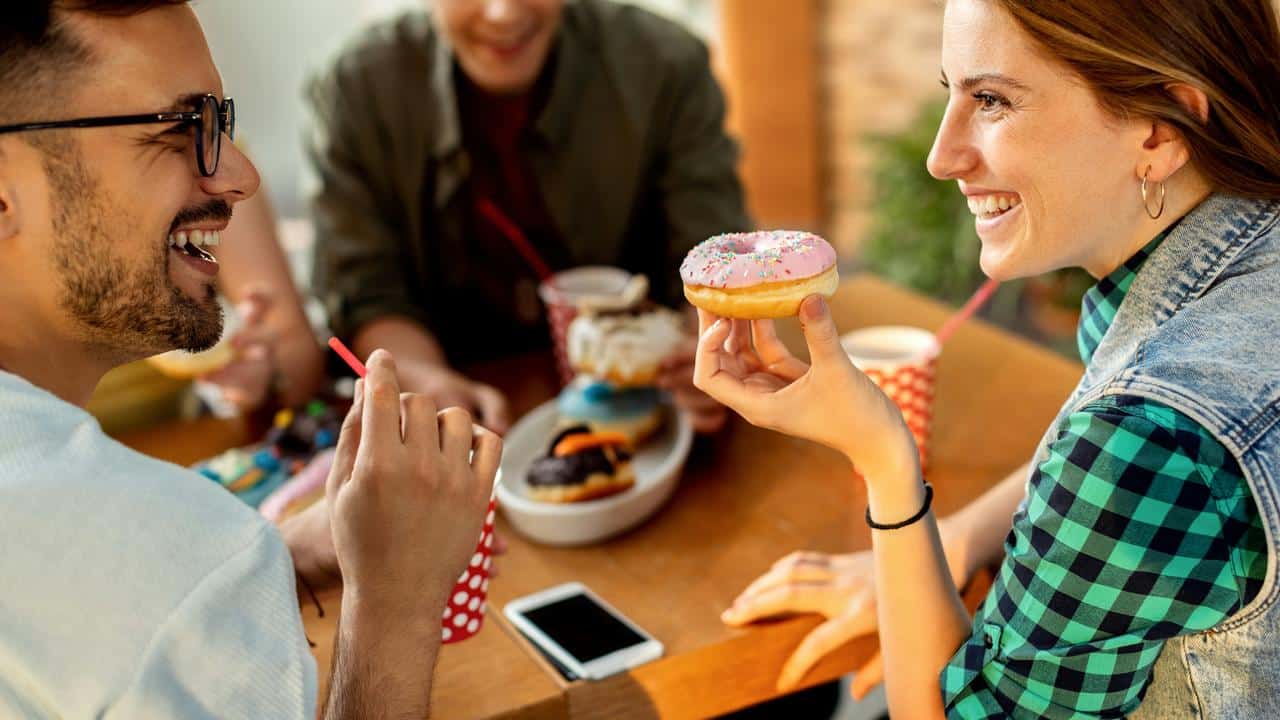 A man and a woman smile at each other while eating outside.