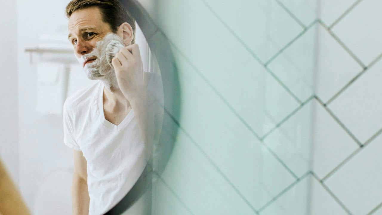 A man shaving in a bathroom mirror.