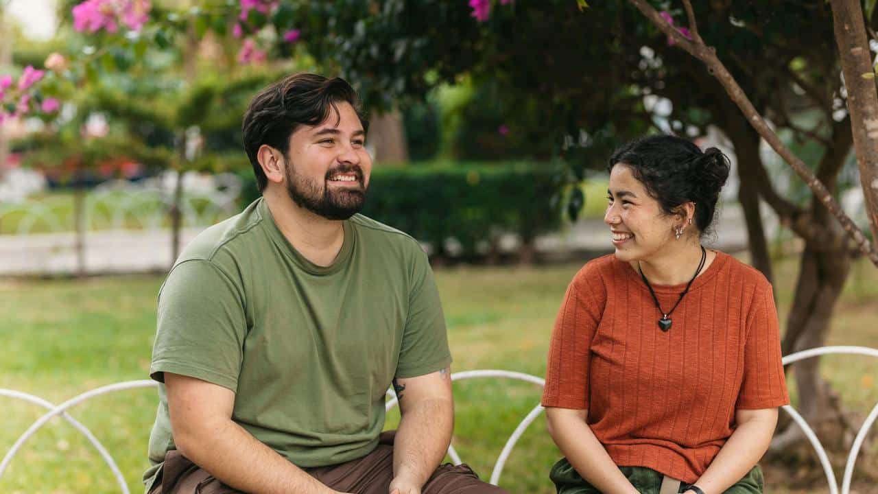 A photo of two people sitting on a bench, smiling at each other.