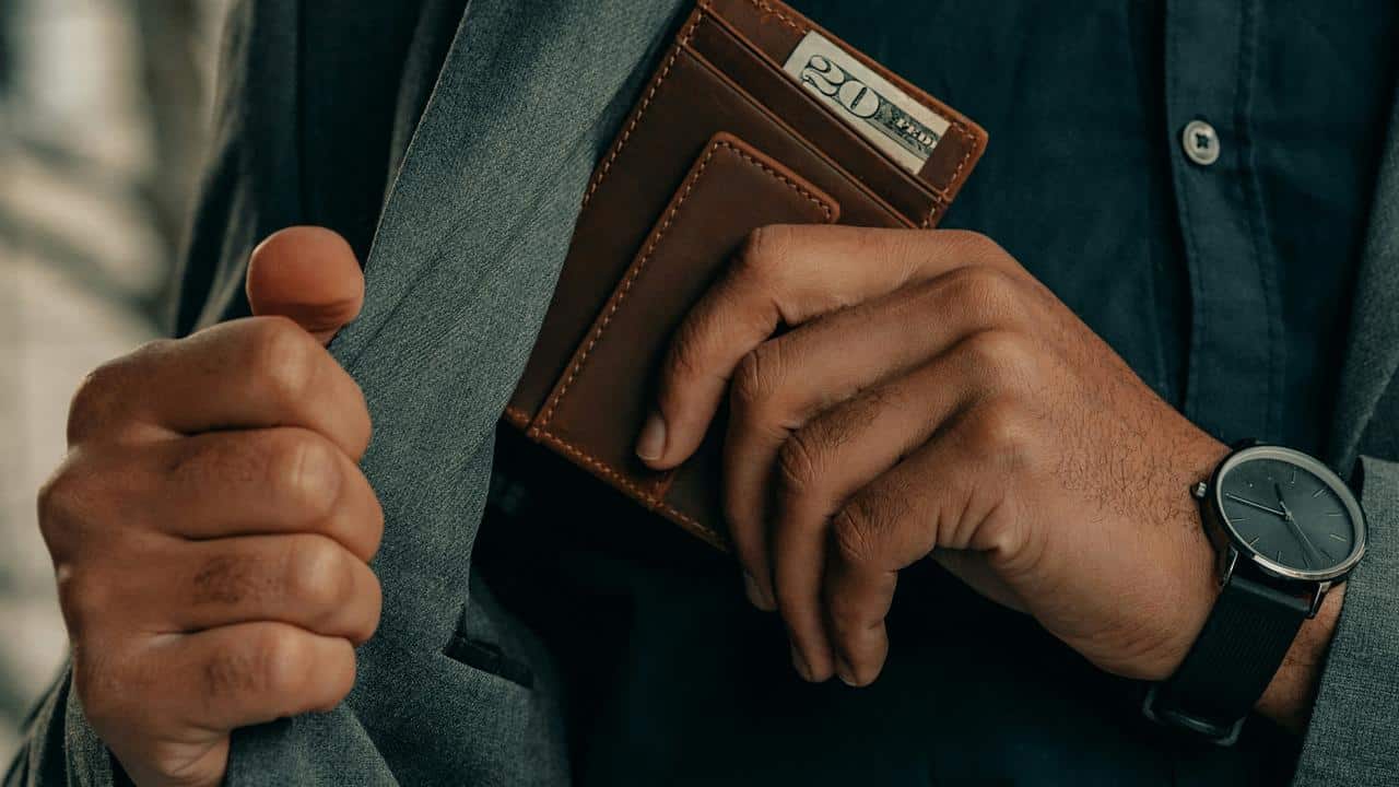 A person putting a wallet into a jacket pocket.