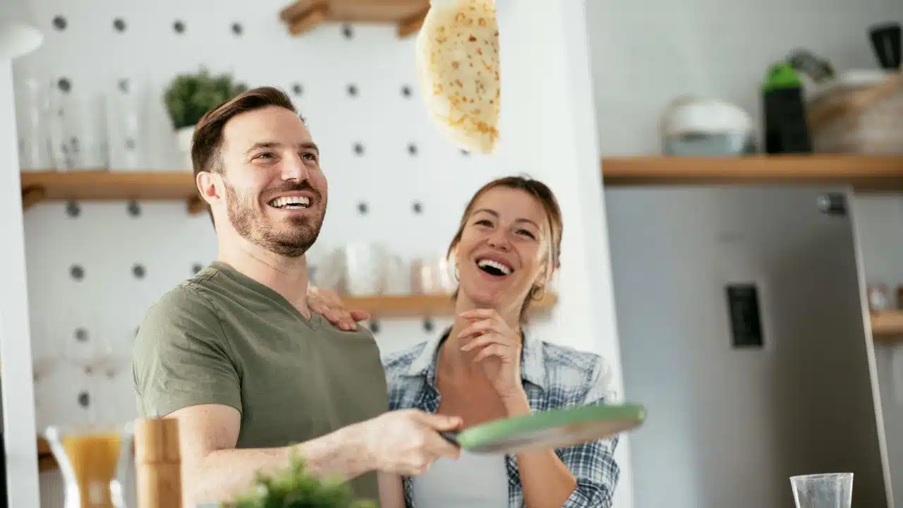 A couple flipping a tortilla and laughing in a kitchen.