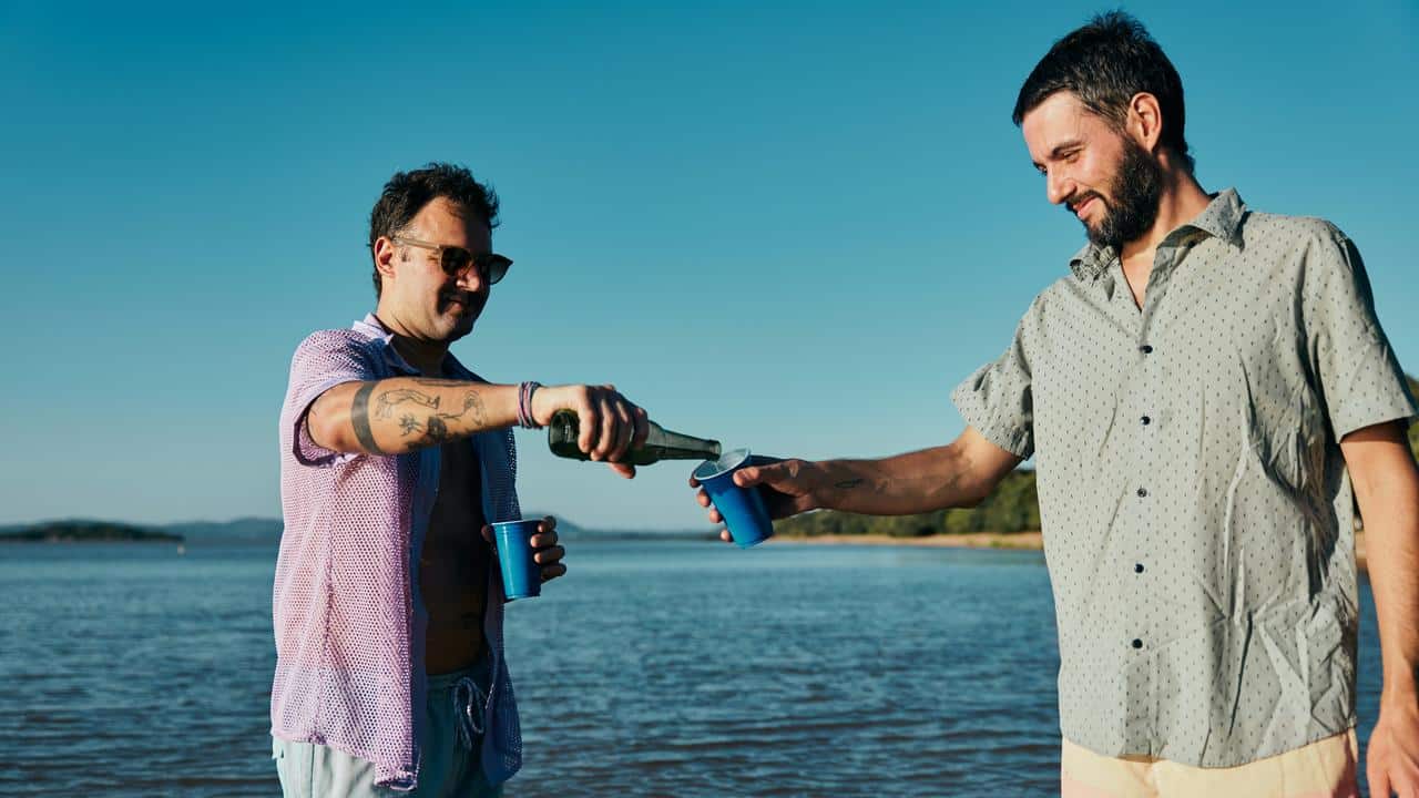 An image of two men enjoying drinks together on a beach.