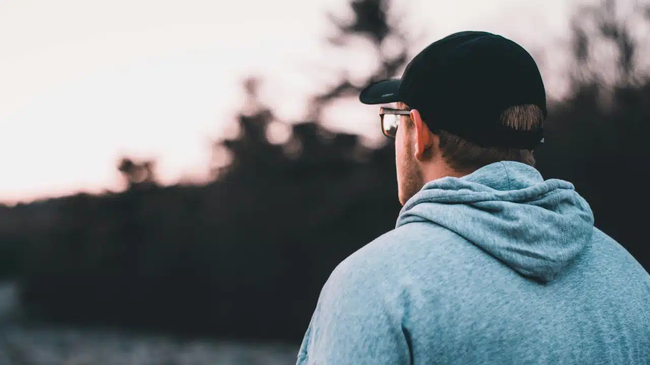 A man in a hoodie and cap looking at the sunset.