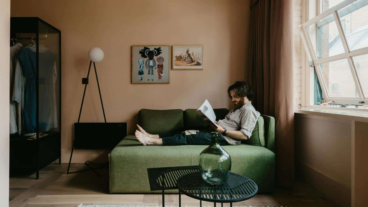A man lounging on a green couch reading a magazine.