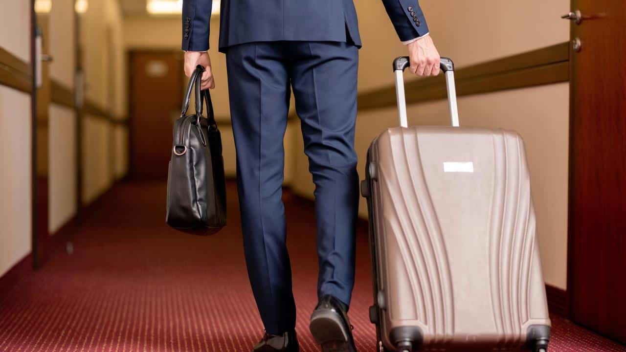 A man in a suit walking with luggage down a hallway.