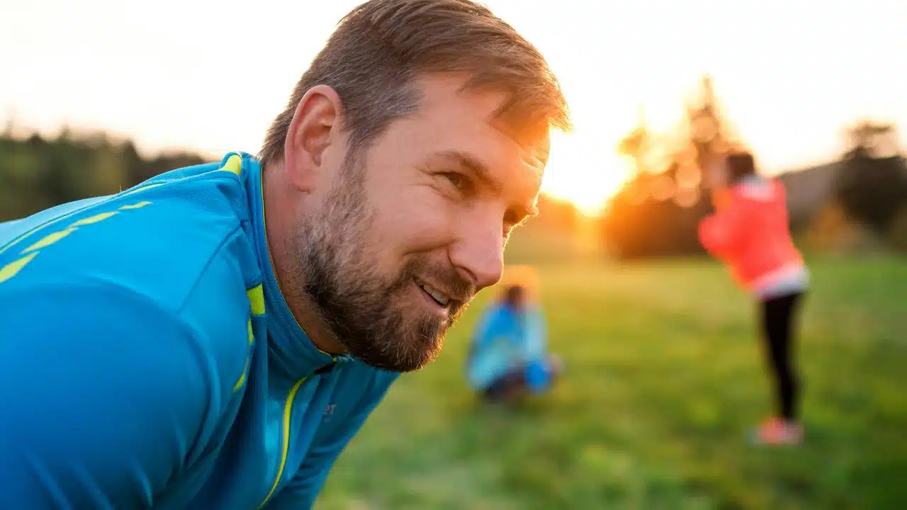 A man in sportswear smiling outdoors at sunset.