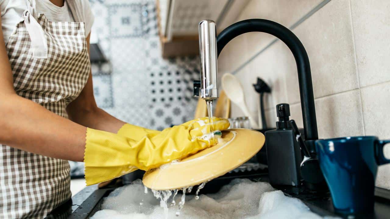 A person washing dishes while wearing yellow gloves.