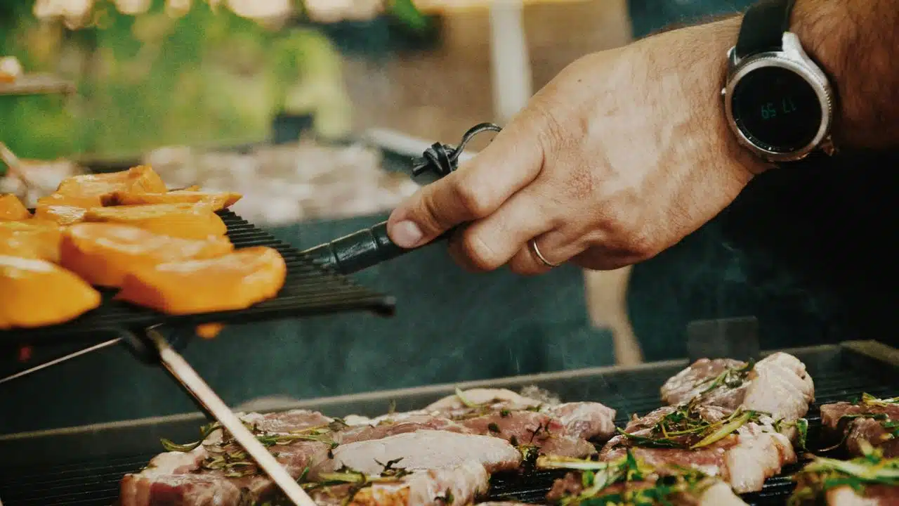 A person grilling meat and vegetables.