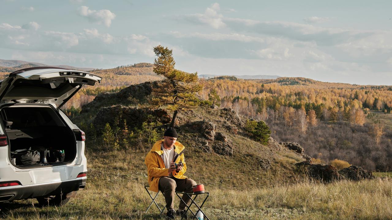 A man camping beside a car in the mountains.