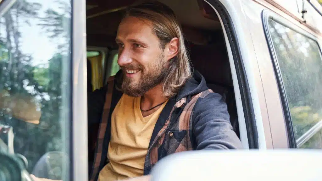 A bearded man smiling in a vehicle.