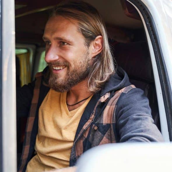 A bearded man smiling in a vehicle.