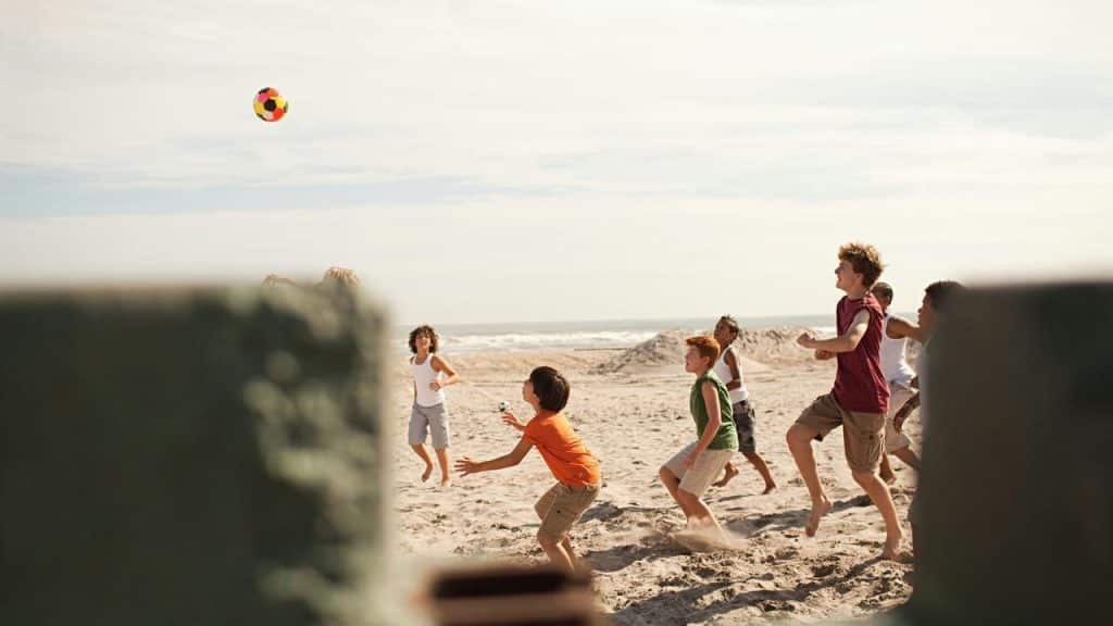 A group of kids playing with a colorful ball on a sandy beach.