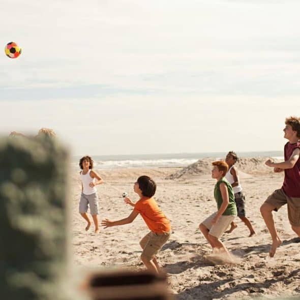 A group of kids playing with a colorful ball on a sandy beach.