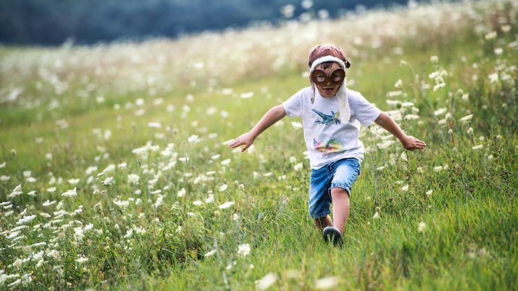 A young boy wearing aviator goggles running through a field of wildflowers.