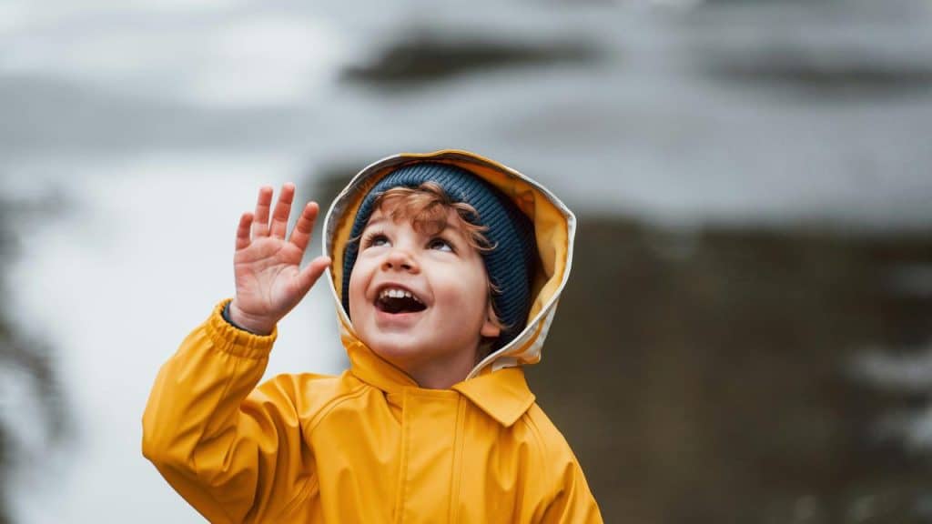 A smiling child in a yellow raincoat looking up and waving.