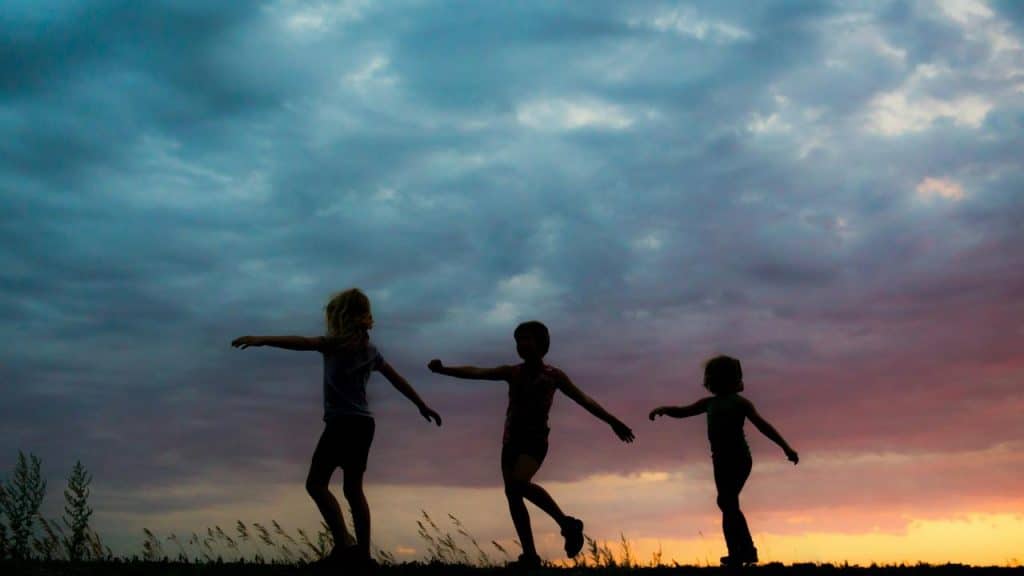 A silhouette of three children playing outdoors at sunset.