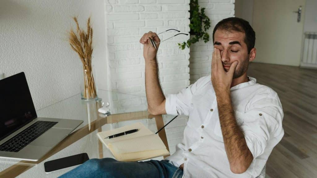 A tired man rubbing his eyes at a desk.