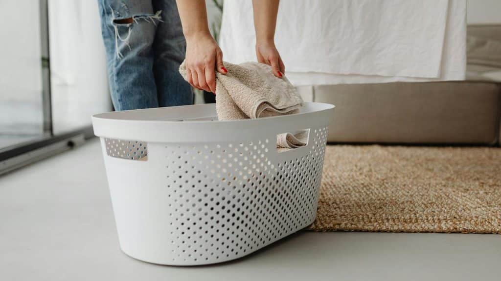 A person placing a folded towel into a white laundry basket.