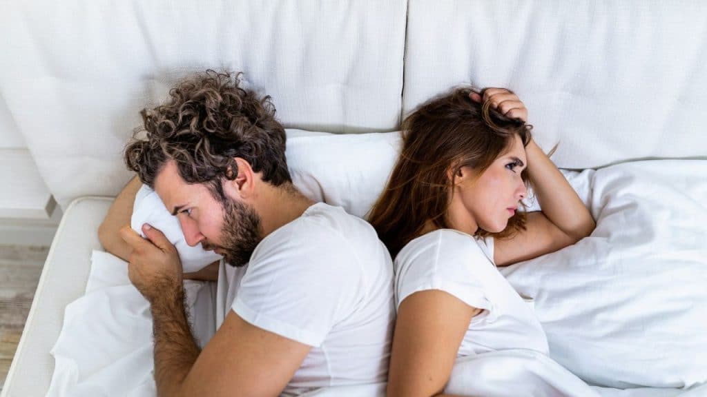 A couple lies in bed back-to-back, seemingly upset with each other.