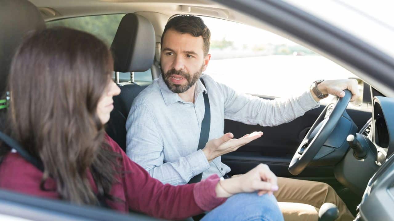 A man behind the wheel of a car is arguing with a woman in the passenger seat.