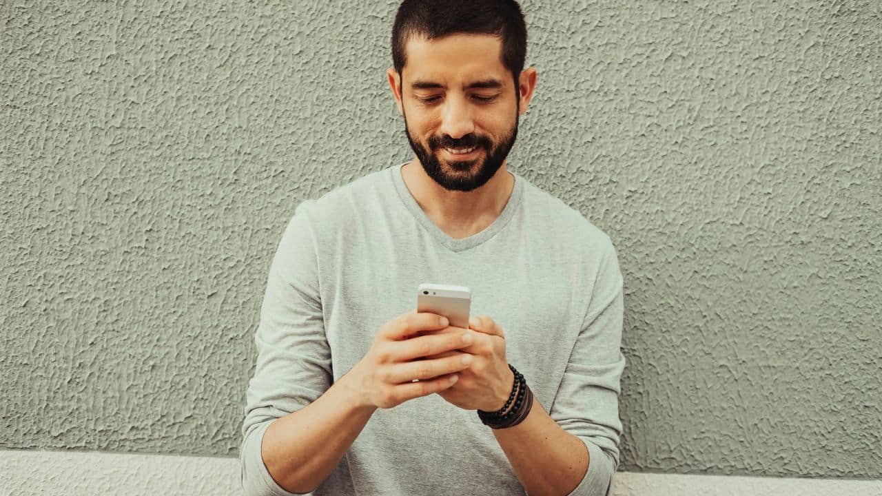A smiling man with a beard is looking down at his phone.