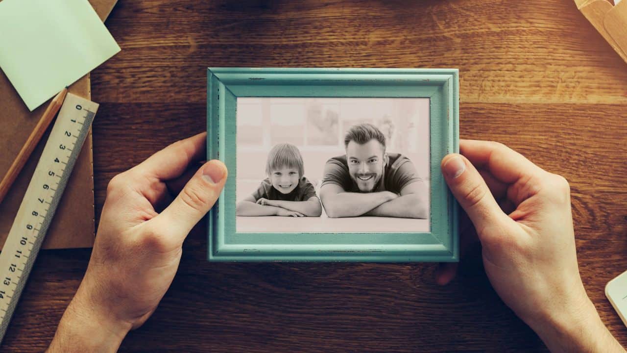 A person's hands hold a photo frame with a black and white photo of a father and son.