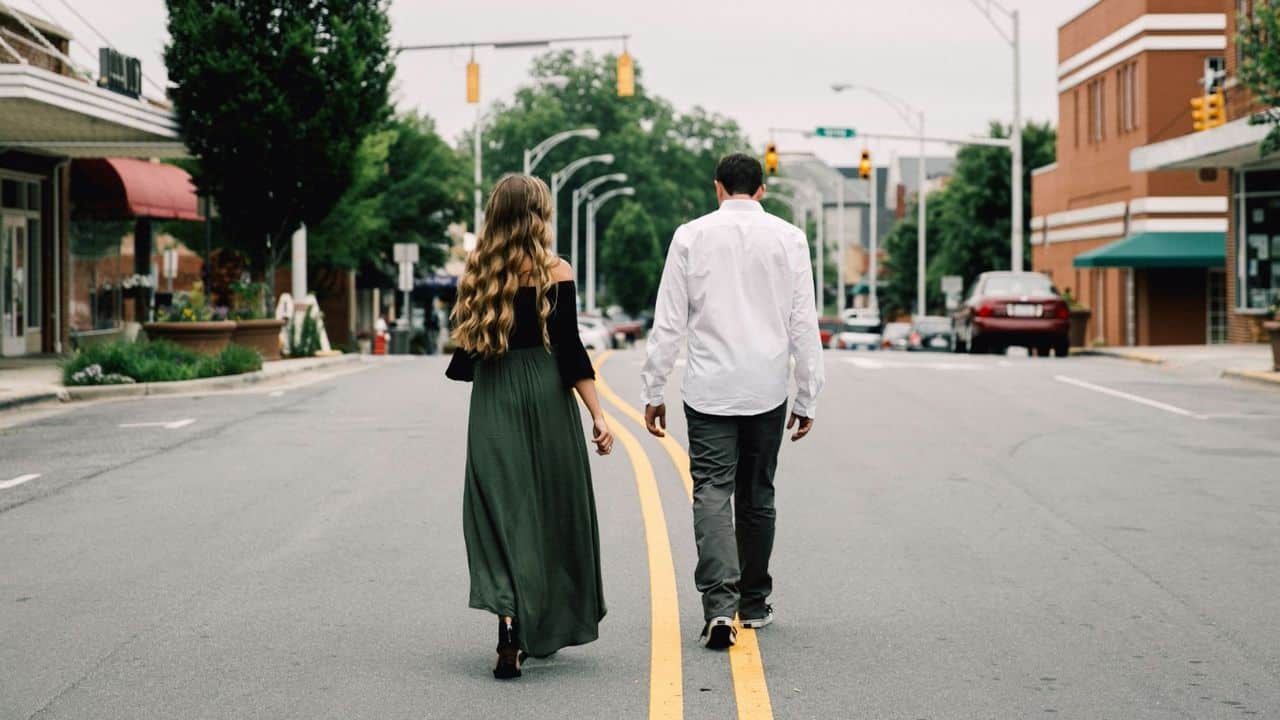 A man and woman walk away from the camera down the middle of a street.