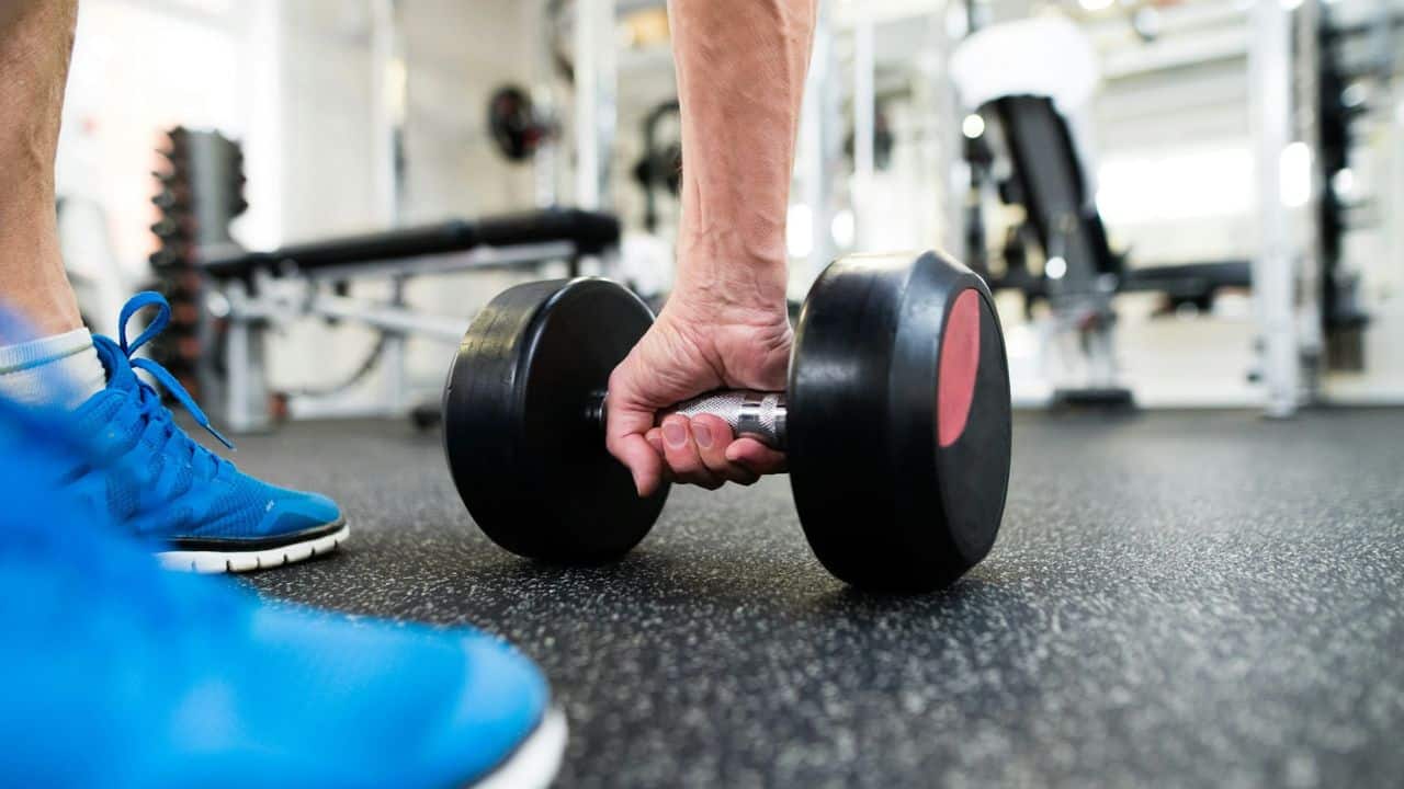 A person's hand picks up a heavy dumbbell from the gym floor.