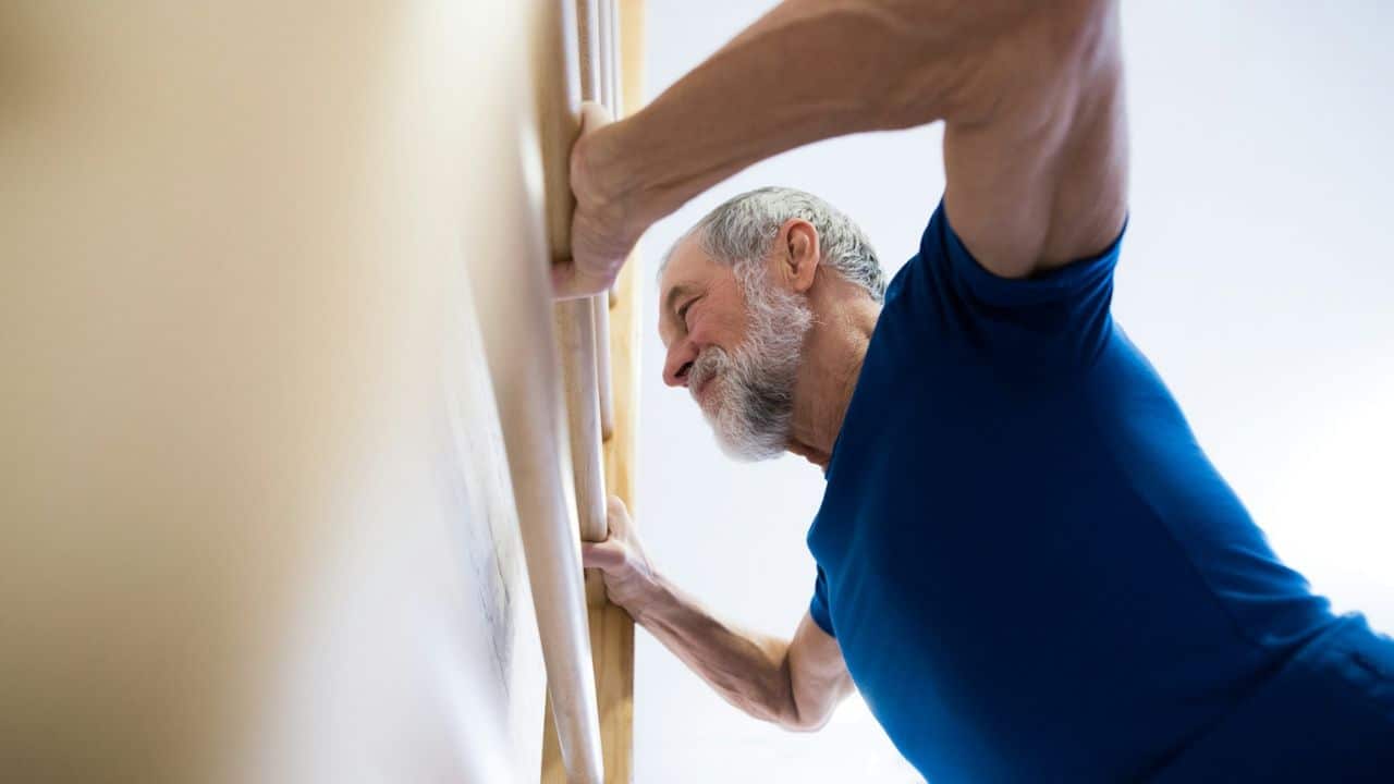 A determined, bearded older man in a blue shirt climbs a wall ladder.
