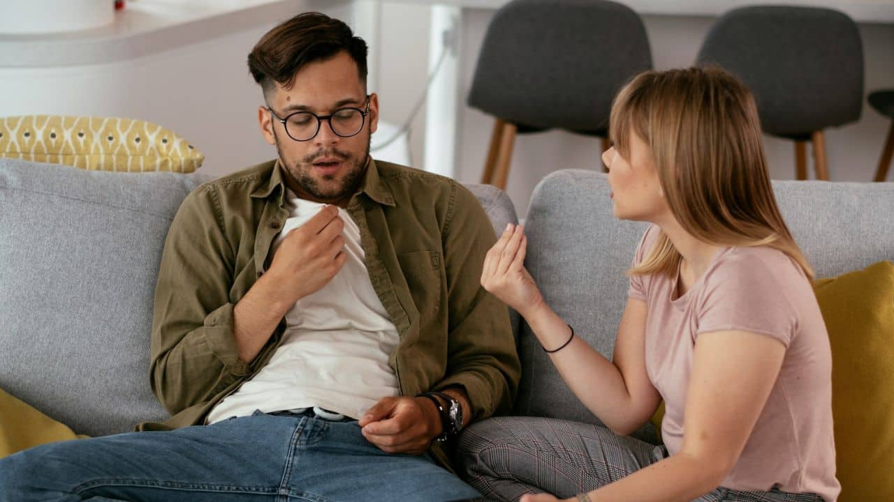 A woman talks animatedly to a man who looks distressed on a couch.