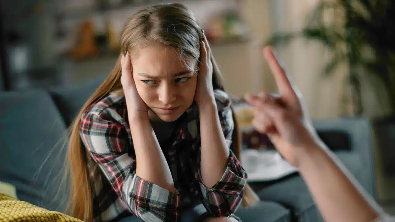 A person covers their ears while a hand points a finger at them.