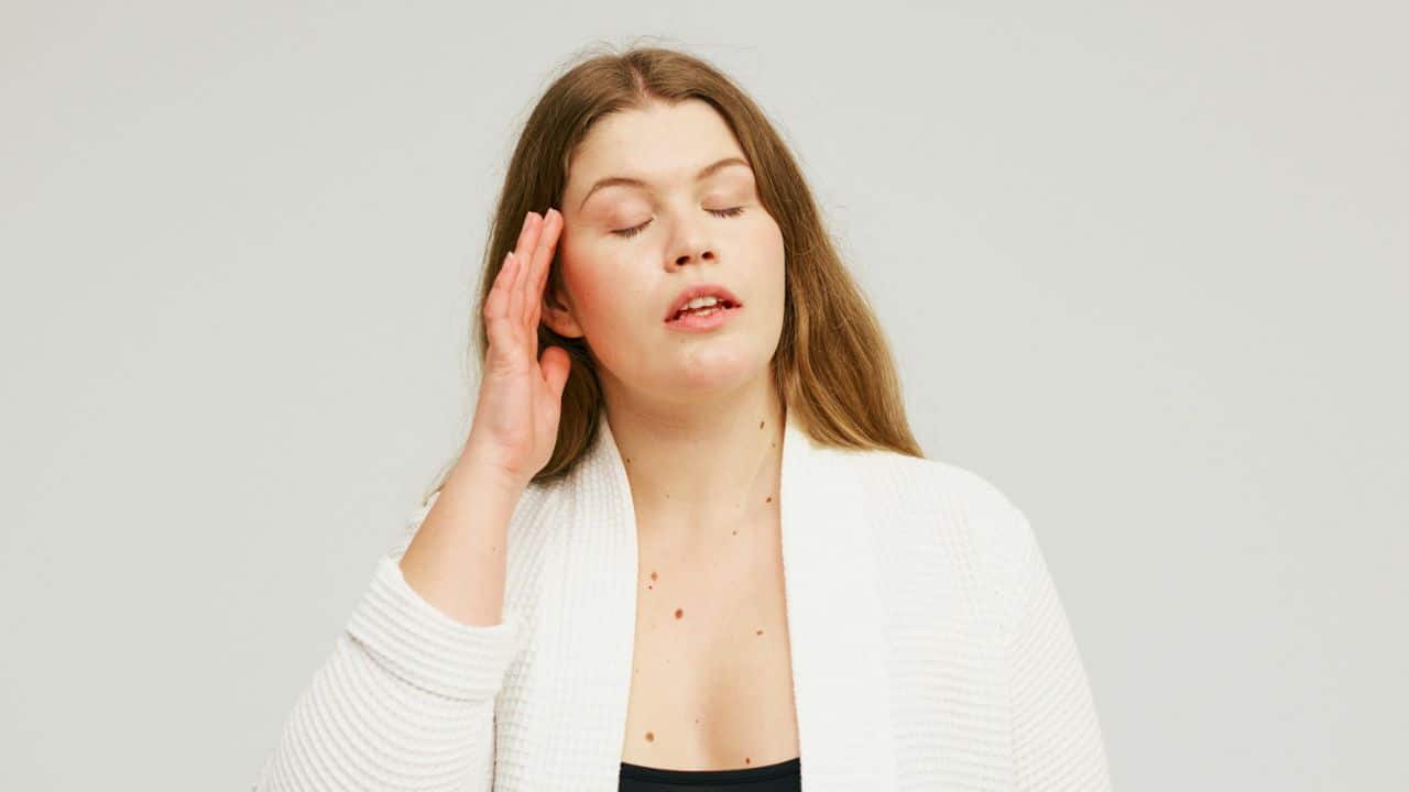 A woman with her eyes closed and a hand on her head looks frustrated.