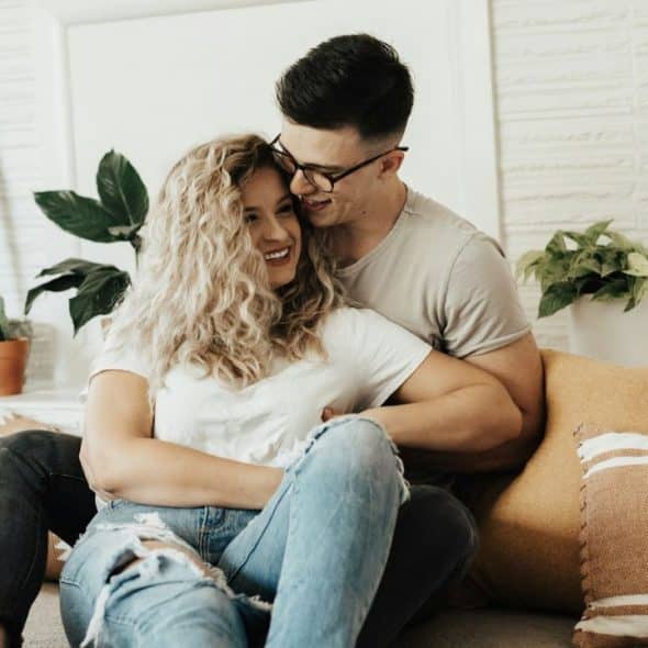 A happy couple embraces on the floor, surrounded by houseplants.