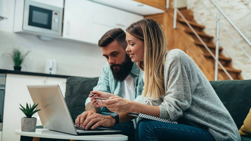 A bearded man and a woman look at a laptop together, appearing to be shopping.