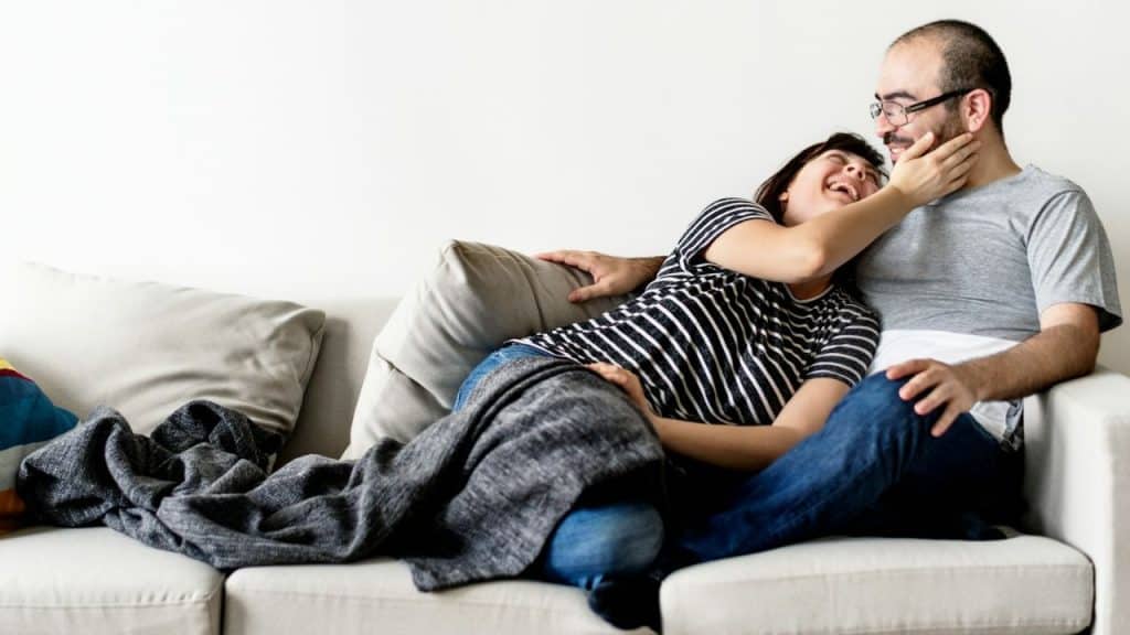A happy couple is snuggling on a couch, looking at each other.