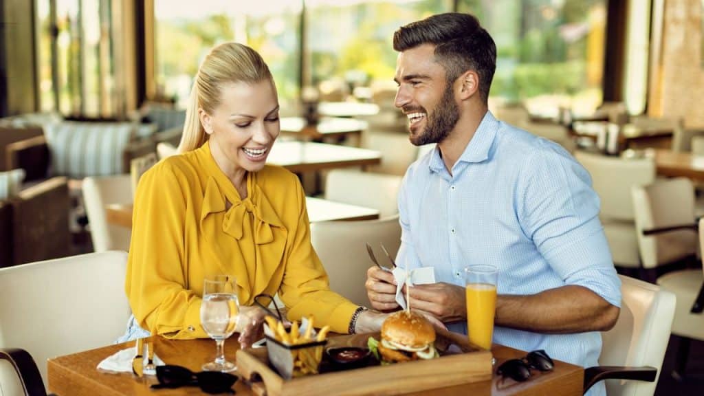 A laughing couple eats together at a restaurant table.