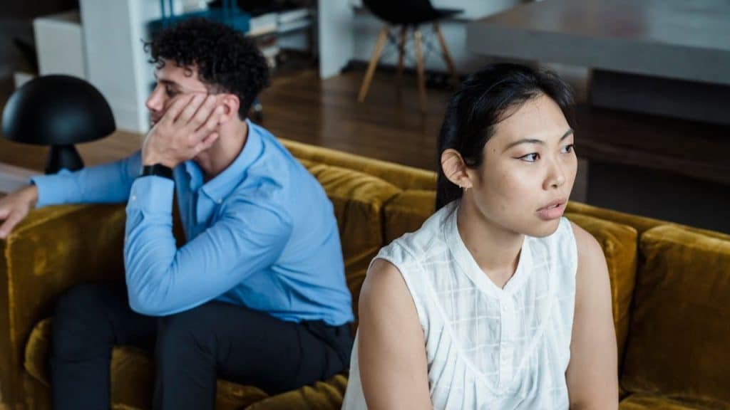A distressed man and woman sit on a couch, looking in opposite directions.
