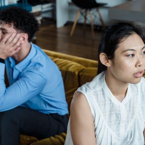 A distressed man and woman sit on a couch, looking in opposite directions.