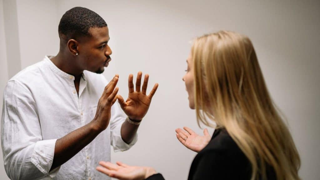 A man and a woman argue with their hands up, facing each other.