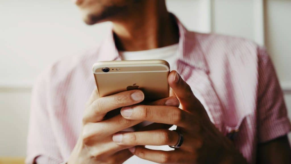 A person in a pink shirt holds and looks at a gold iPhone.