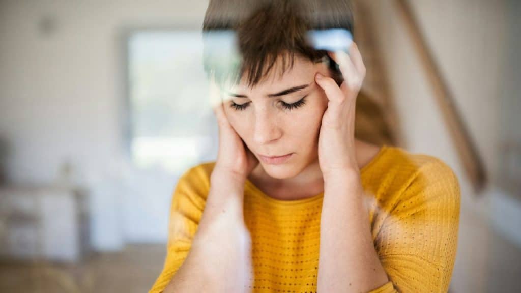 A woman with her eyes closed and hands on her head looks stressed.