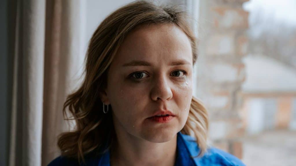 A sad woman with tears on her face looks directly at the camera.