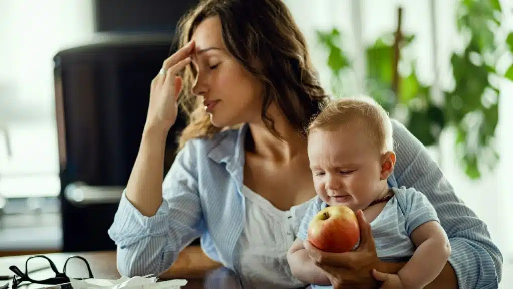 A frustrated mother holds a crying baby, who is holding an apple.