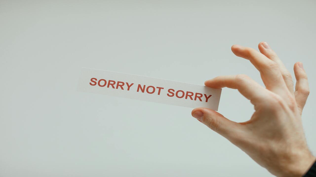 A hand holding a “sorry not sorry” sticker.