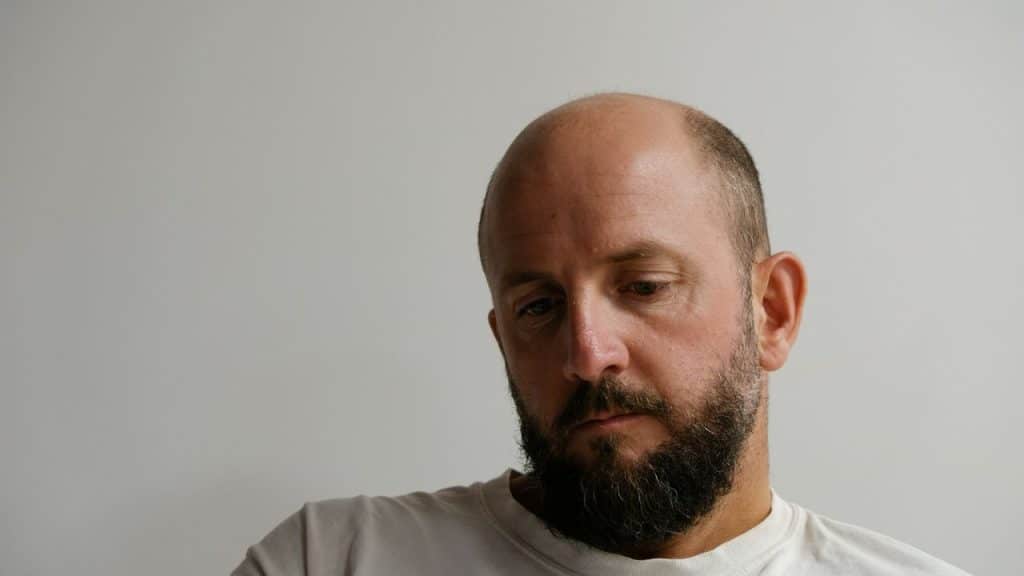 A close-up of a bald man with a beard, looking down thoughtfully.