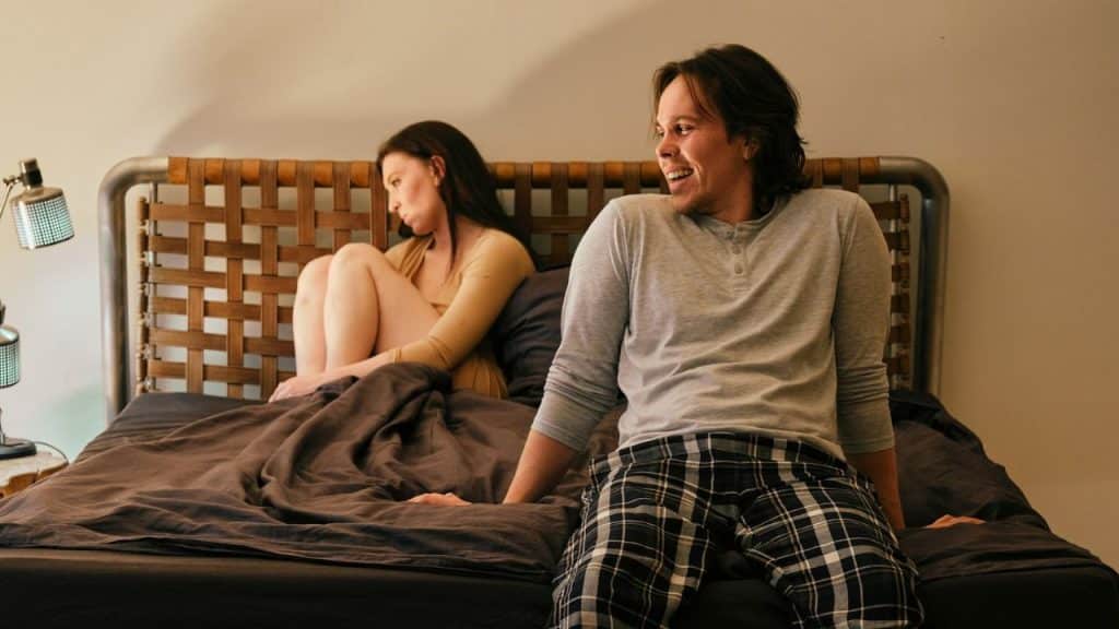 A man smiles and looks to the right while a woman looks away from him on the bed.