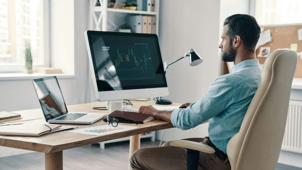 A professional man sits at his desk, focused on his computer screens.